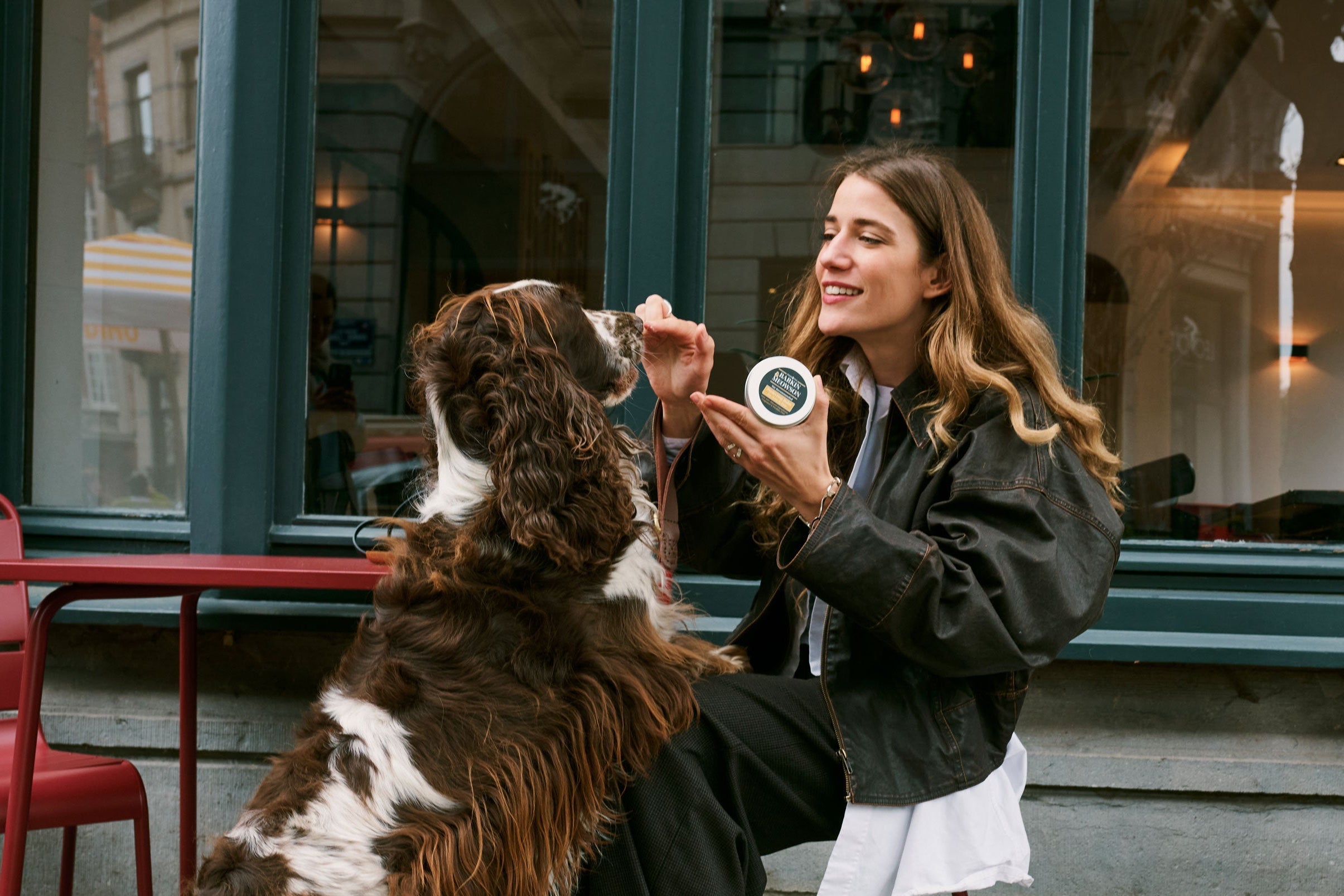 Woman sitting with a dog at an outdoor cafe, holding a coffee cup.