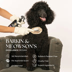 Black dog being groomed with a brush, wearing gloves holding grooming products, on a neutral background.